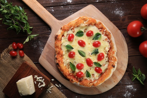 Her ses en margarita pizza ligge på et pizzabræt klar til severing