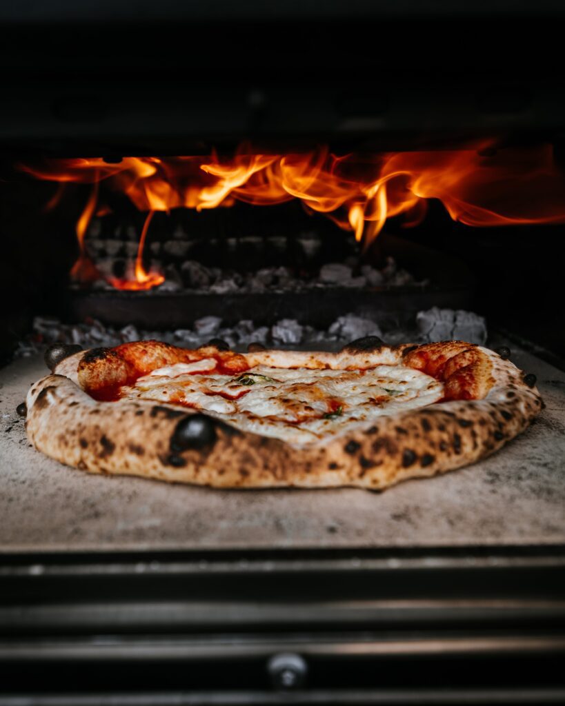 Her kan du få hjælp til at finde den helt rigtige pizzaovn til brænde. På billedet ses en pizza på vej ind i en pizzaovn på bræde