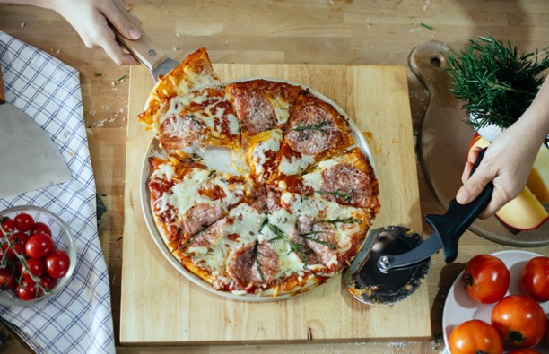 Et billede af en lækker pizza med en pizzaskærer, der netop har skåret pizzaen i slides.