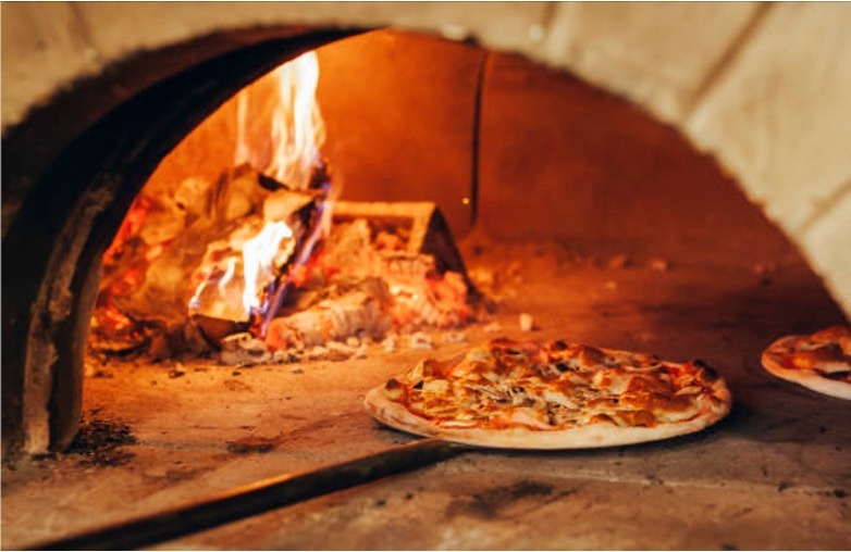 På billedet ses en pizza på vej ind i en stenovns pizza ovn